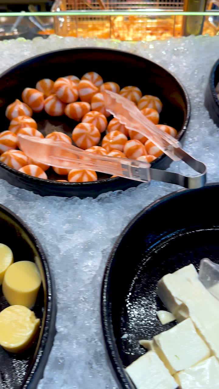 Vari tofu, torte di pesce, polpette di gamberi e noodles disposti sul ghiaccio sotto una luminosa illuminazione da buffet.