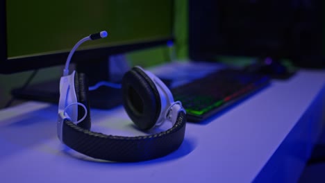 close-up, the gamer's headphones are on the computer table. modern headphones with a microphone, a backlit keyboard and a large monitor, a gaming space. 4k, prores