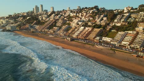 Vista-Aérea-Volando-Por-El-Paisaje-Urbano-Dorado-De-Reñaca-Frente-Al-Mar-Con-Un-Retiro-Turístico-Soleado-En-La-Playa