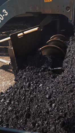 metal construction of a heavy paver machine pouring out hot asphalt on the road. asphalt spreader at work. large truck laying black bitumen. close-up. vertical video