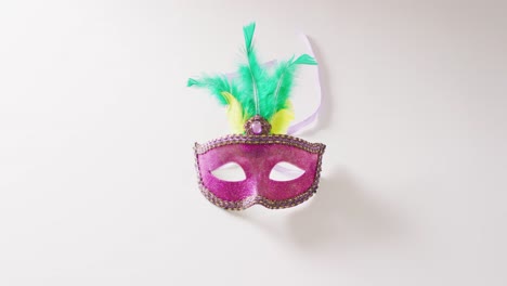 Video-of-pink-masquerade-mask-with-green-and-yellow-feathers-on-white-background-with-copy-space