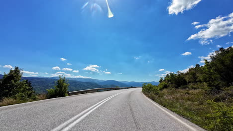 Vista-Desde-El-Punto-De-Vista-De-Un-Conductor-De-Una-Carretera-Rural-Que-Conduce-A-La-Grecia-Urbana-En-Un-Día-Claro-Y-Soleado