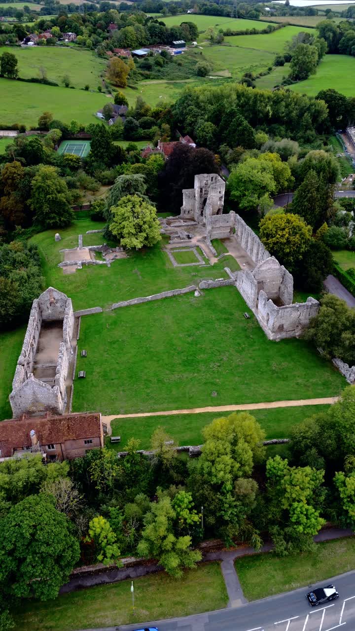 Riprese aeree grandangolari con drone che sorvola da sinistra le rovine del palazzo di Bishop's Waltham, catturando le storiche mura in pietra, gli alberi autunnali circostanti e la calda luce dorata del tramonto per una vista panoramica del villaggio
