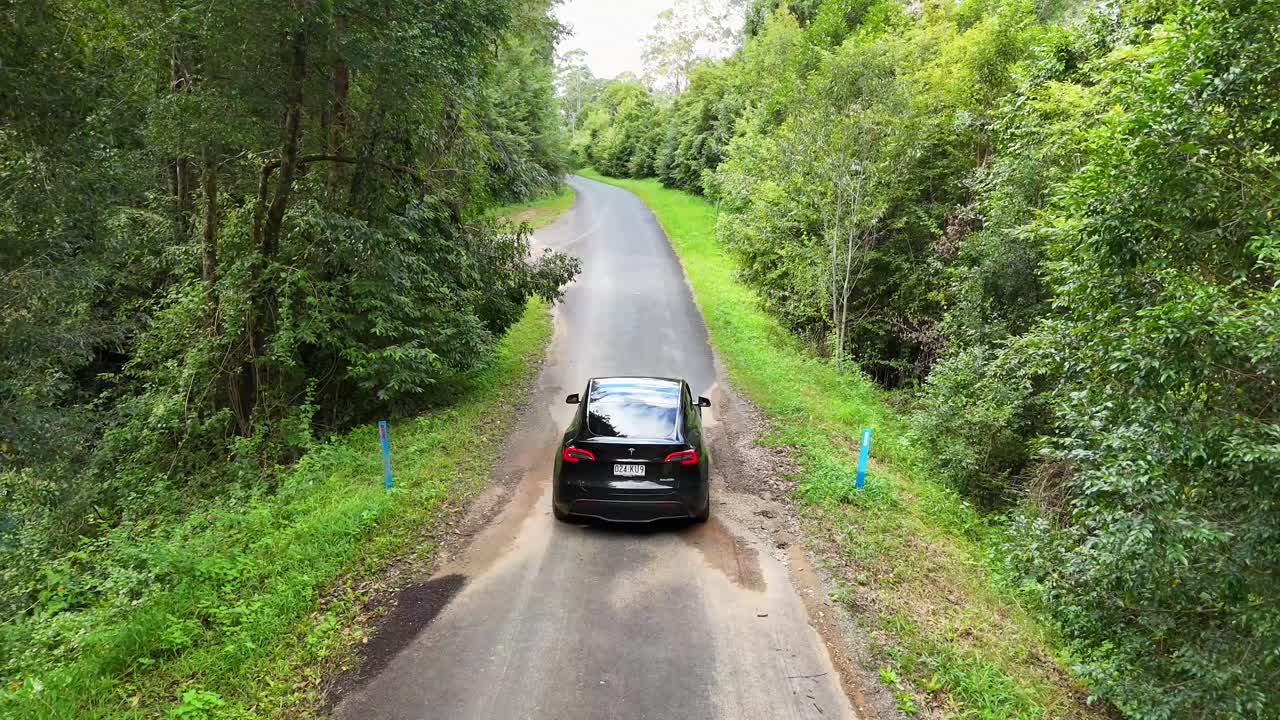 A car navigates a winding road through dense greenery in Bellingen, Australia, under natural daylight, capturing serene rural landscapes