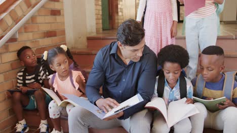 maestro masculino diverso y niños sentados en las escaleras leyendo libros en la escuela primaria, cámara lenta