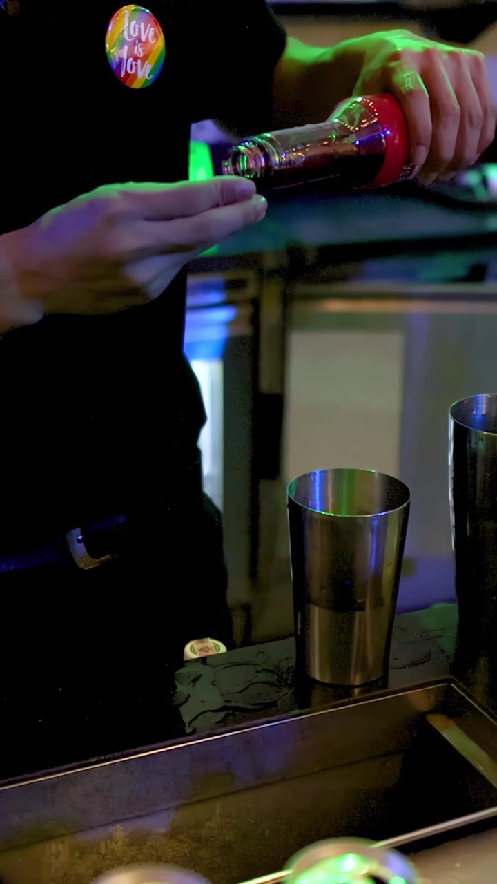 Barman prepara un cocktail rosso usando uno shaker in un bar di Bangkok illuminato al neon, primo piano, telecamera fissa