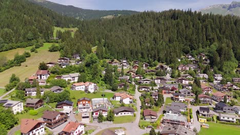 picturesque swiss village with houses and homes located on mountainside. sunny day with green fields and fir trees. aerial flyover shot