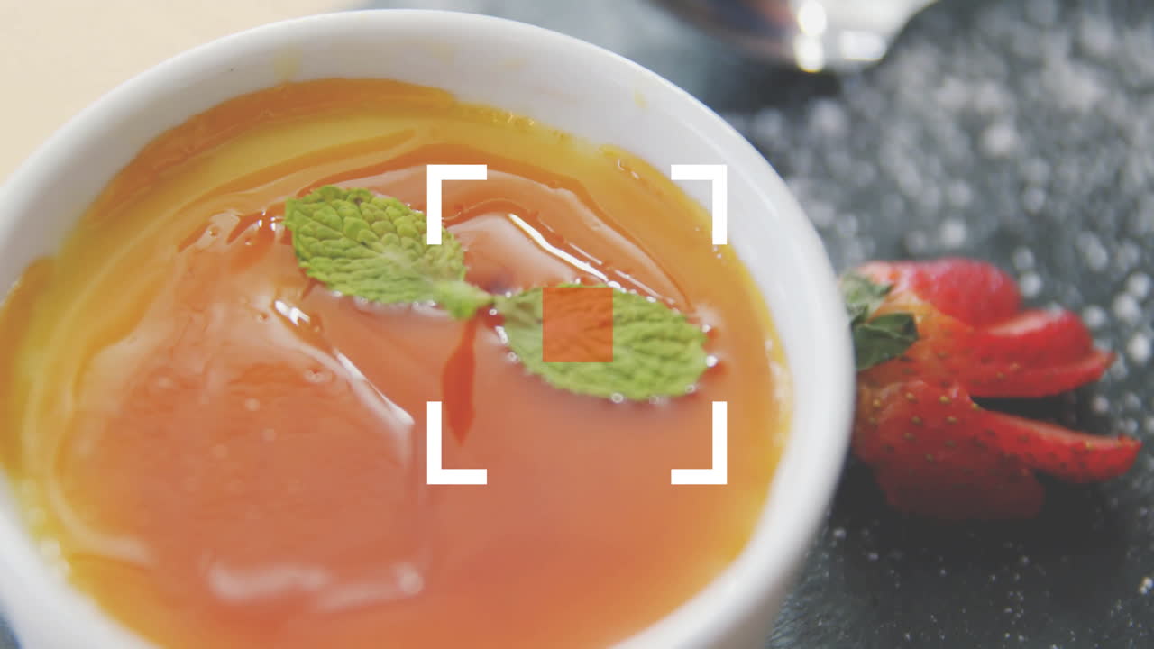 Garnishing caramel dessert with mint leaves, sliced strawberry beside on plate
