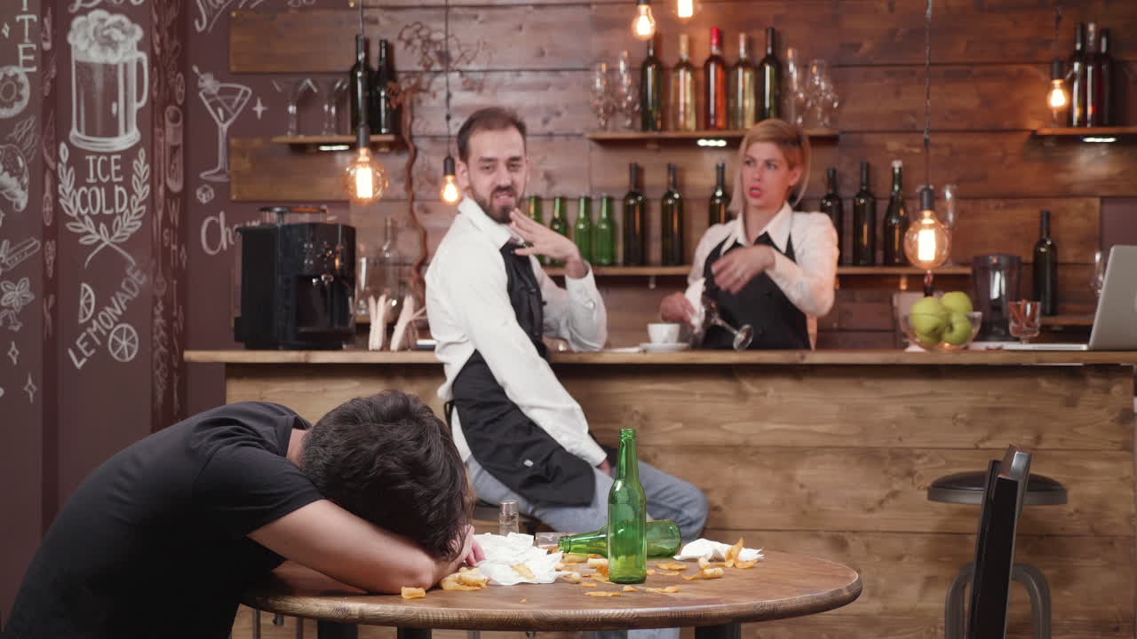 Drunk man at a bar with bartenders working in the background