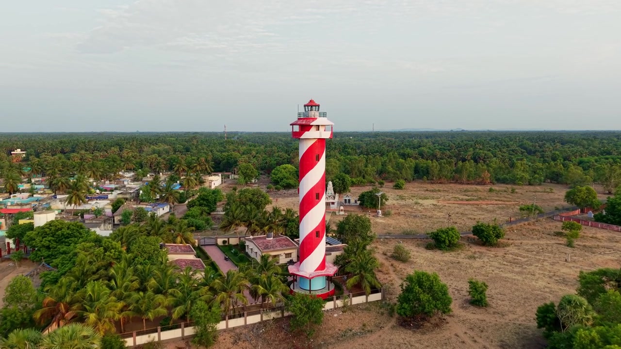 Ripresa aerea con drone di un faro a strisce rosse e bianche, circondato da lagune, mangrovie e vegetazione lussureggiante vicino a Chennai nel Tamil Nadu, India