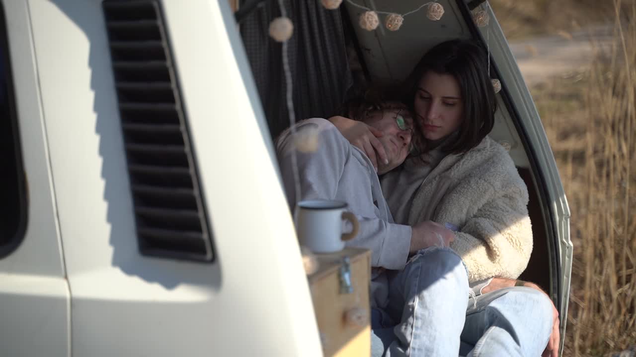A young couple in love embracing in the back of a caravan by a lake.