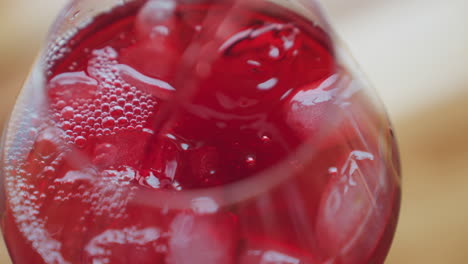 close up of vibrant red wine pouring into transparent glass filled with ice cubes, creating bubbling effect and rich texture as chilled drink swirls around frozen pieces in refreshing motion