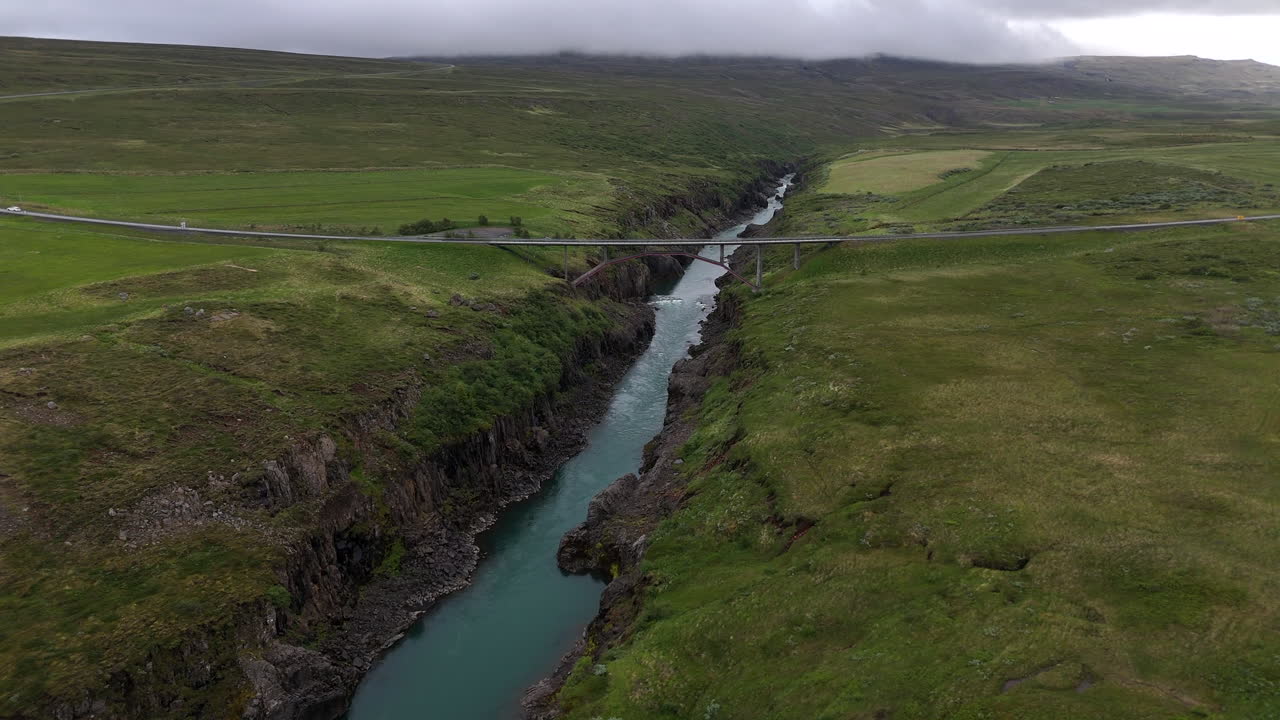 Aerial view of the Jökulsá River bridge in Iceland, showing flowing water, surrounding rugged terrain, and wide open landscape under clear sky
