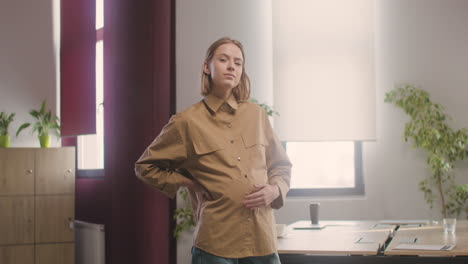 Pregnant-Happy-Woman-Posing-At-Camera-While-Touching-Her-Belly-In-The-Office-1