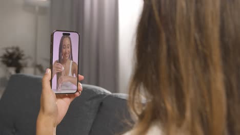 primer plano de una mujer sentada en el sofá en casa mirando el video de demostración de un producto de belleza en un teléfono móvil 1