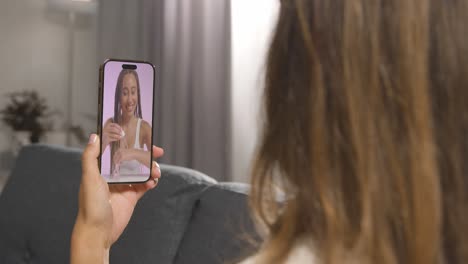 close up of woman sitting on sofa at home looking at beauty product demonstration video on mobile phone 1