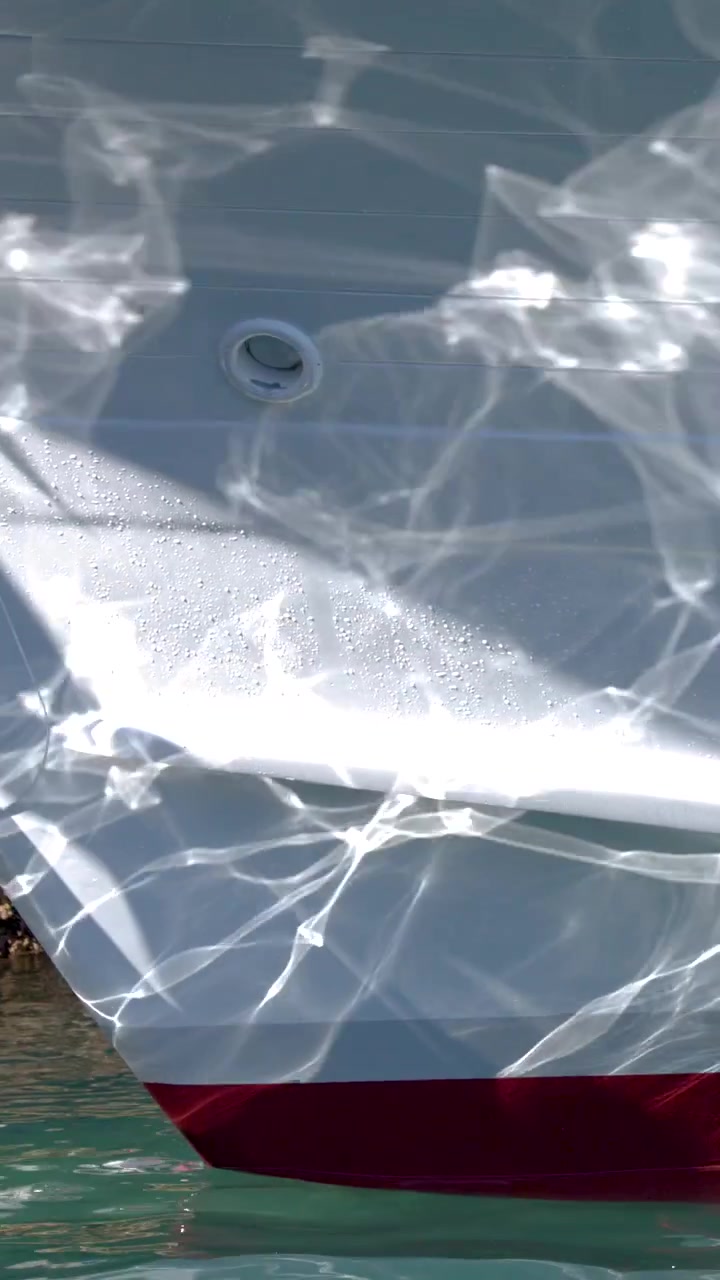 Close-up shot of shimmering water reflections dancing across a white boat hull in sunlight.