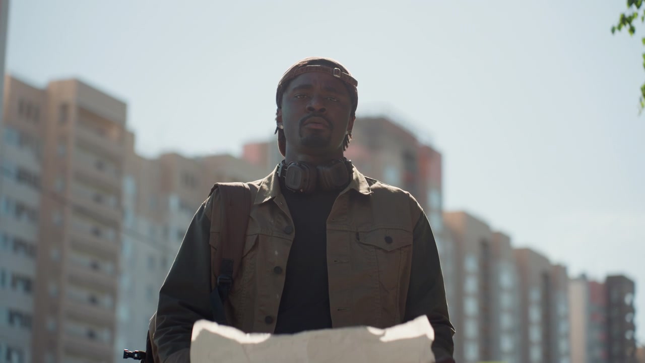 Close up of man holding large paper with shadow standing outdoors in urban environment. Man wears brown jacket and cap background features tall buildings under clear sky