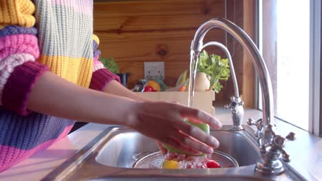 Mid-section-of-african-american-woman-rinsing-vegetables-in-sunny-kitchen,-in-slow-motion