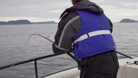 norwegian fisherman with a rod fishing from the boat in an open sea in norway - medium shot