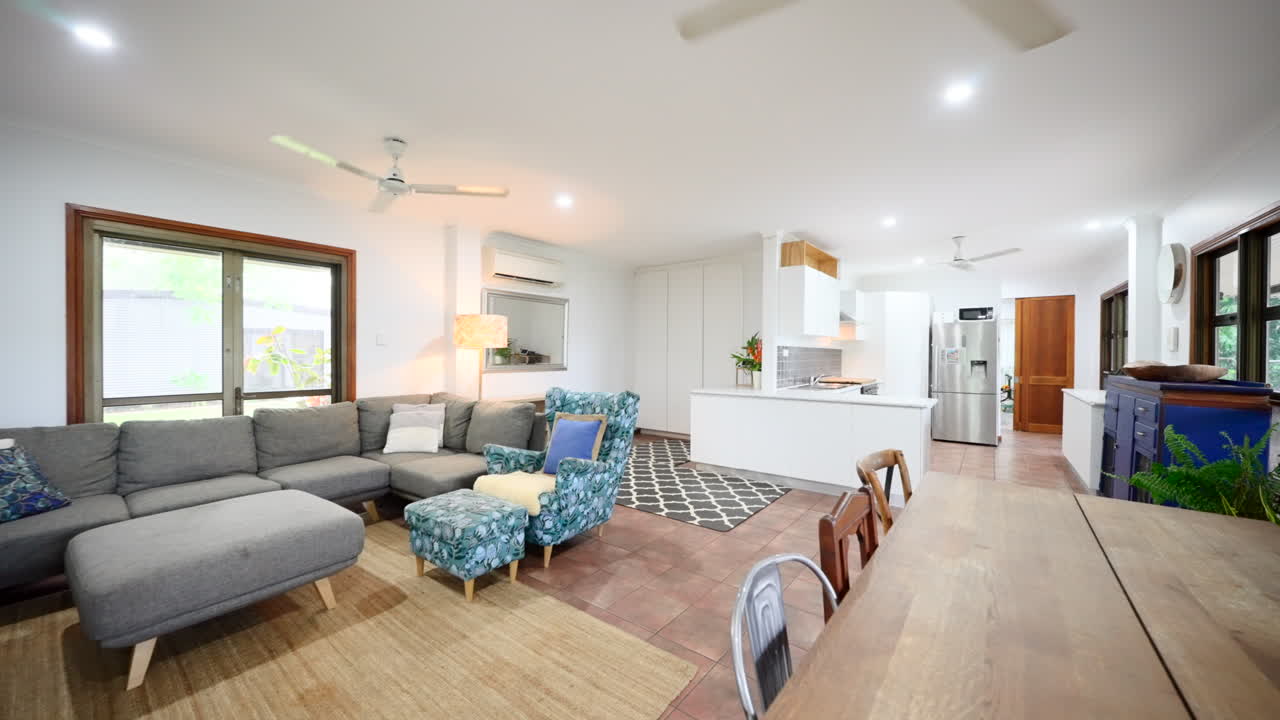 Wide angle pan establishes lived in mismatched cute furniture of living room area and kitchen of house