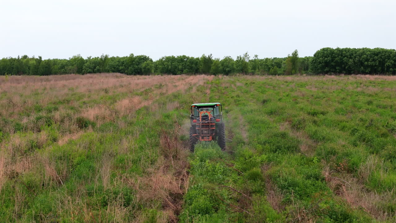 Aerial drone shot of tractor spraying fertilizer while moving through farmland.