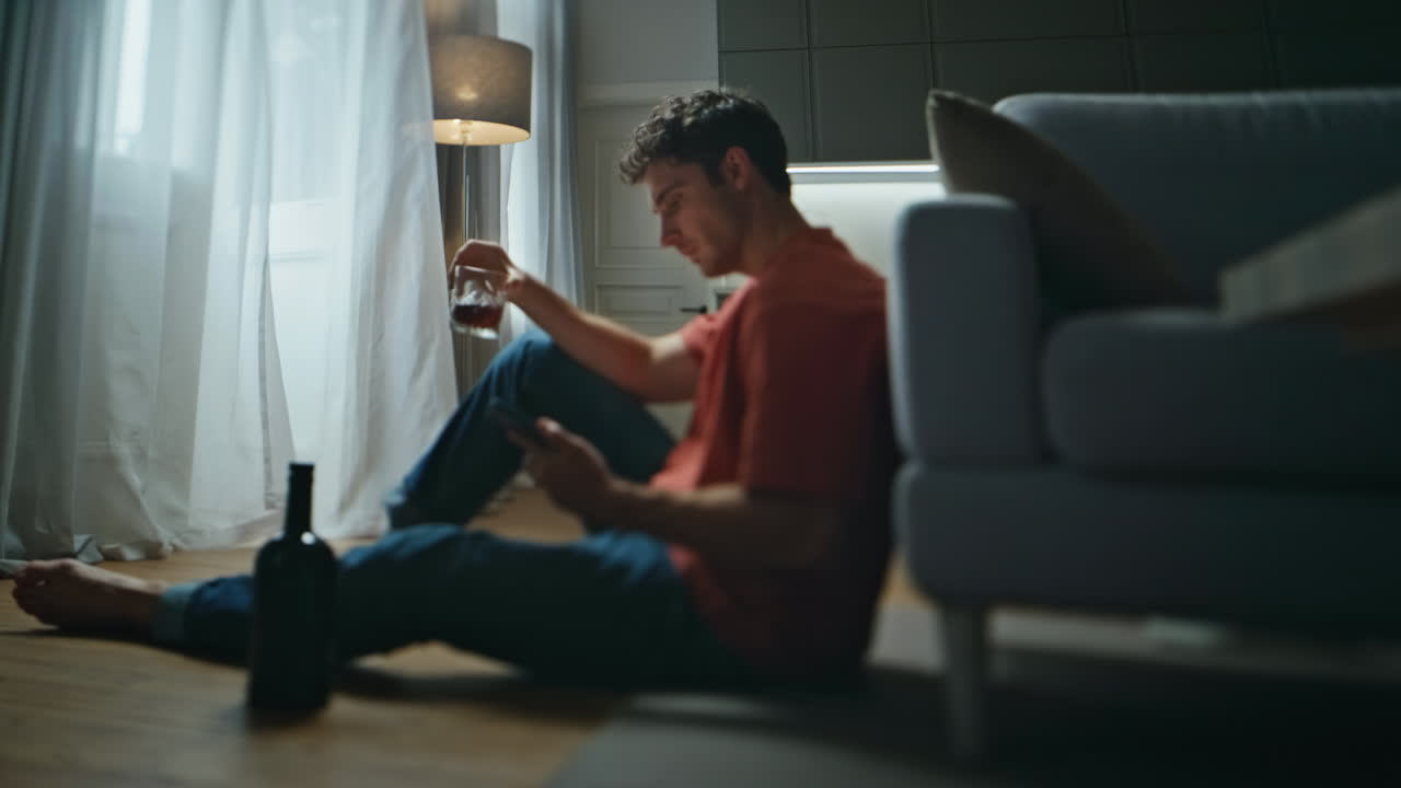 Lonely alcoholic drinking whiskey glass alone in room. Breakup man waiting sms
