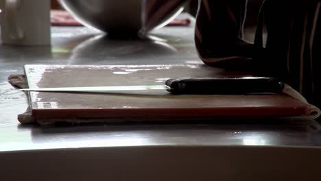 a chef picks up a sharp knife to dry with tea towel and puts knife back down on chopping board, preparing for start of service