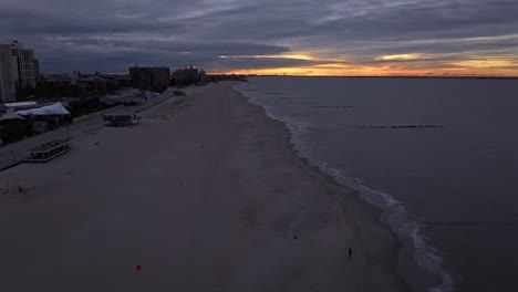 Un-Lapso-De-Tiempo-Aéreo-Sobre-La-Playa-En-Coney-Island,-Ny-Durante-Un-Amanecer-Nublado-Y-Colorido