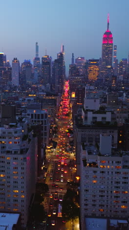 wide new york road with hundreds of cars moving along. descending drone footage over the light street at sun down. vertical video