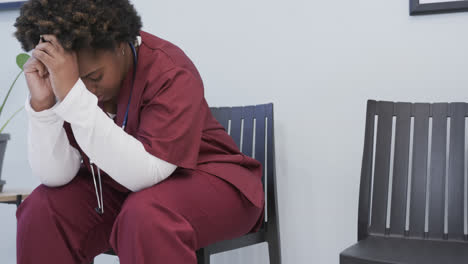 tired african american female doctor sitting in hospital waiting room, slow motion