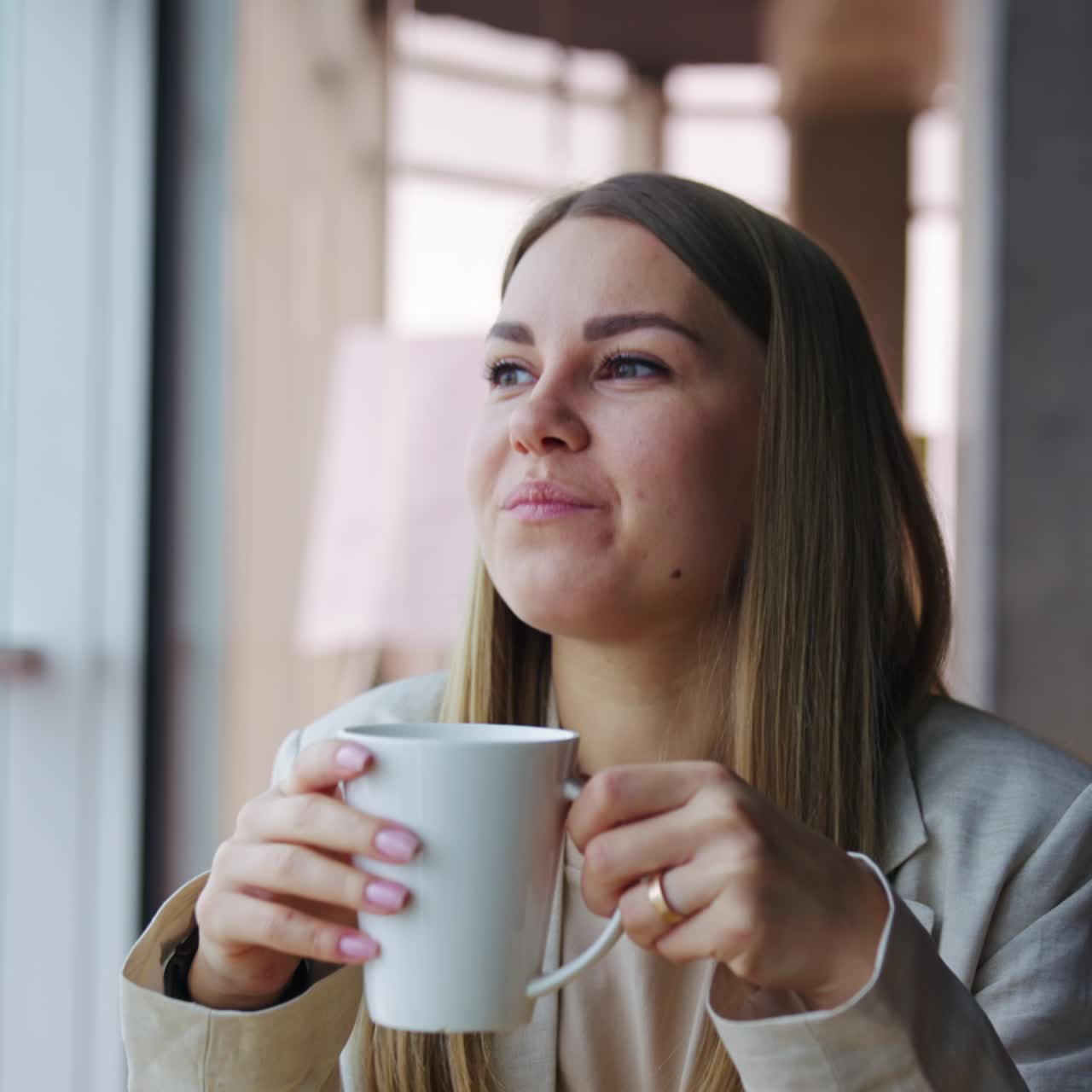 Happy smiling lady enjoys rest and tea during lunch break. Young woman looks dreamily into the window