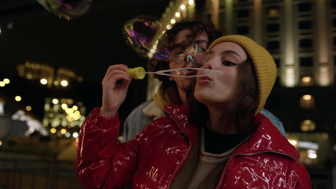 웃는 커플이 야외에서 비누 거품을 불어넣고, 도시 거리에서 데이트를 즐기는 커플.