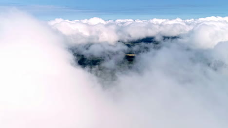 Aerial-view-of-passage-through-white-thick-clouds-on-a-sunny-day-with-green-nature-below