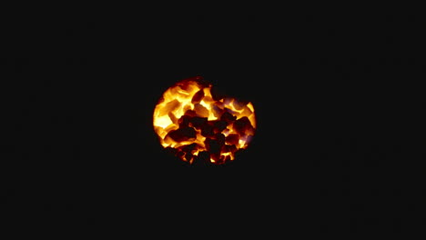 Coals of fire glowing in the dark through a hole, close up shot