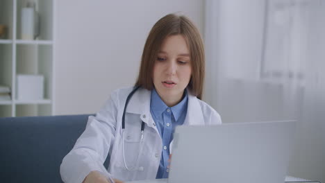 female head physician of hospital is communicating with doctors by online video conference at laptop sitting in her office