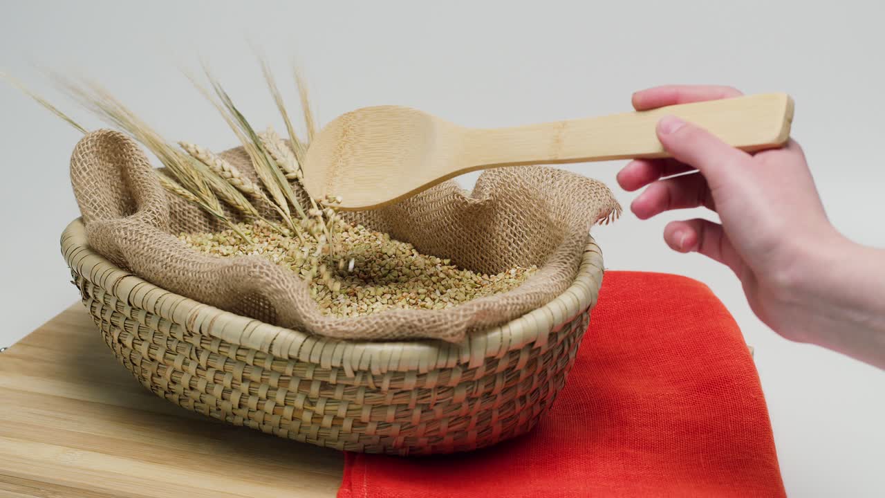 Mano che preleva grano saraceno verde da un cesto di vimini con un cucchiaio di legno