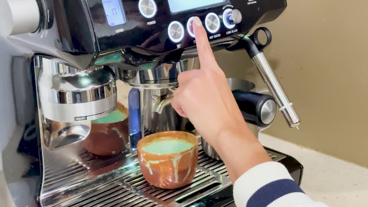 A person operates an espresso machine, preparing a cup of coffee in a well-lit kitchen setting