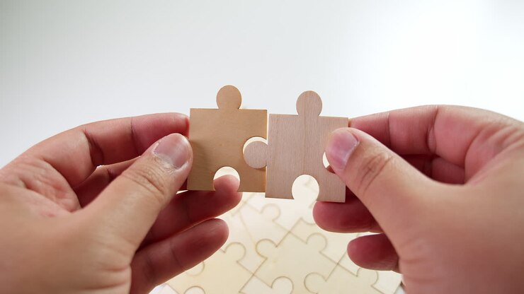 Peças de quebra-cabeça na mesa, então a mão esquerda e a mão direita juntam duas peças, encaixando-as antes de as pousar na mesa