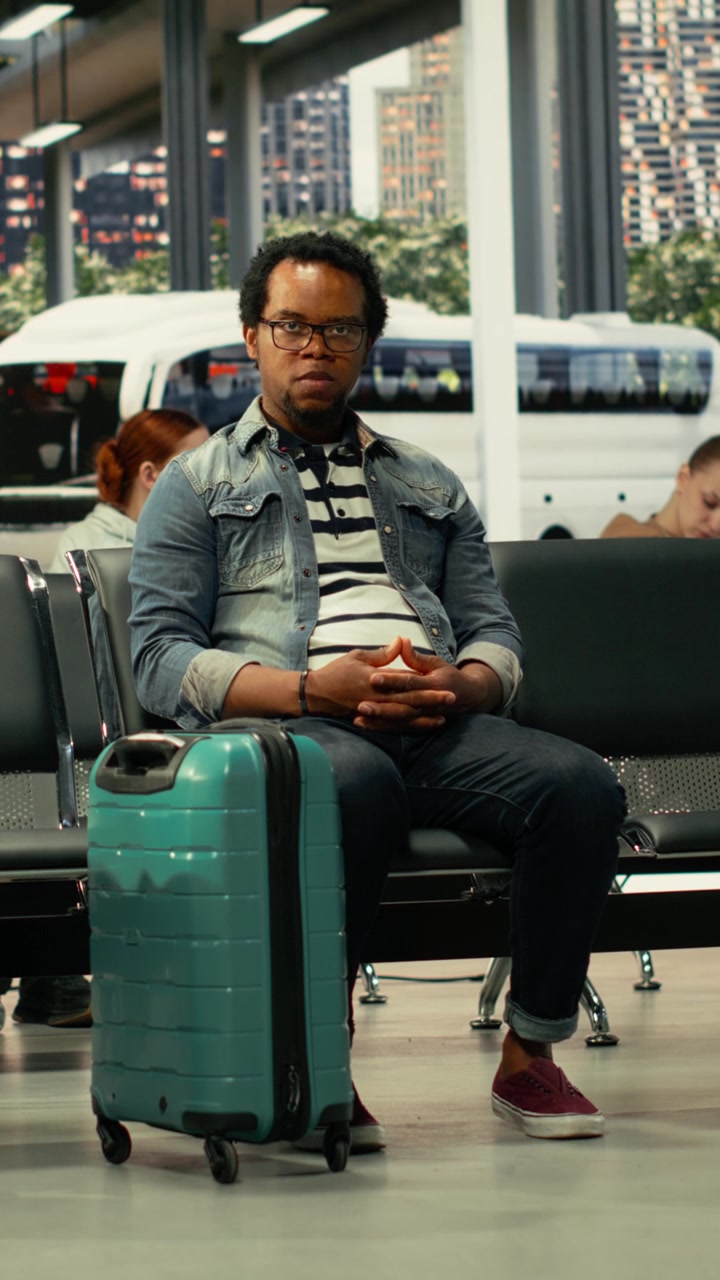 Viaggiatore afroamericano solitario in un terminal degli autobus circondato da passeggeri