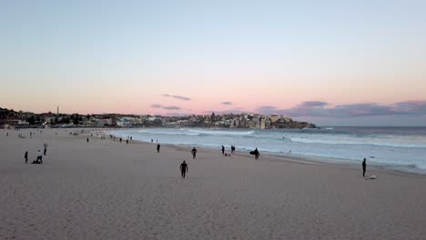 Gente-En-La-Orilla-Arenosa-De-La-Playa-De-Bondi-Con-El-Paisaje-Urbano-Al-Fondo-Durante-La-Puesta-De-Sol-En-Sydney,-Nsw,-Australia