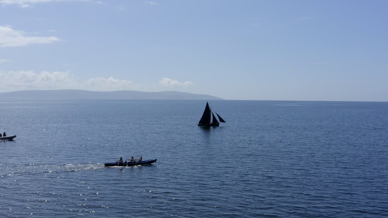 vista de seguimiento de perfil lateral del barco currach y el barco galway hookers en el océano abierto