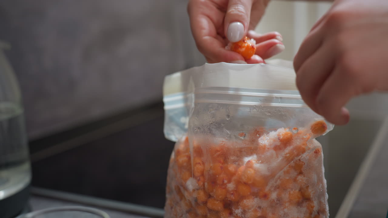 Fingers Adding Frozen Berries Carefully, Preparing Fruit For Preservation On Kitchen Countertop, Hand Transfers Frozen Citrus Berries Into Storage Bag During Meal Preparation In Kitchen
