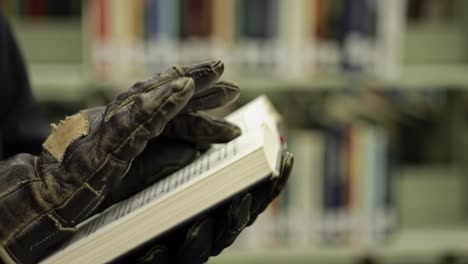 a gloved hand gently reading a book in a library setting, surrounded by shelves filled with books, capturing a moment of contemplation and discovery