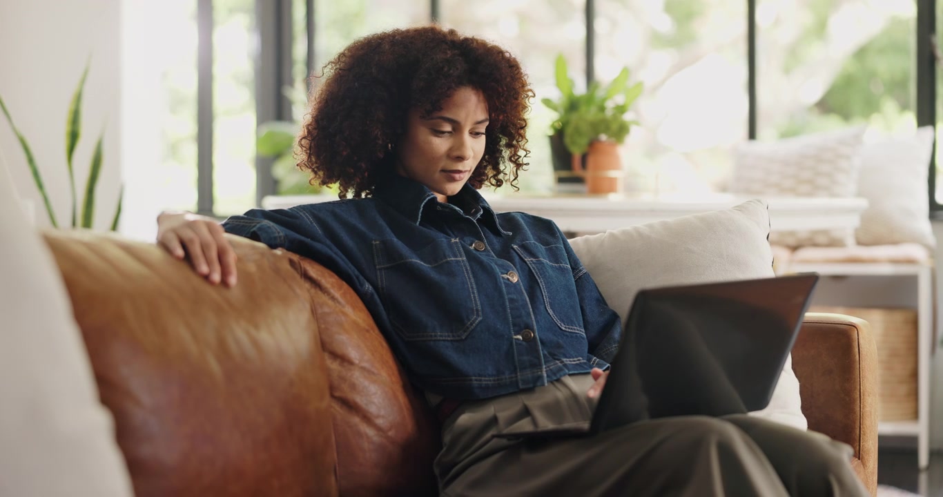 Ung kvinde arbejder på bærbar computer, mens hun sidder på en lædersofa