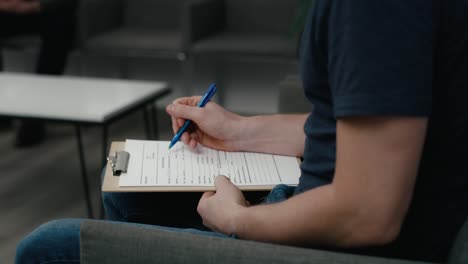 Unrecognizable-man-sitting-in-waiting-room-and-filling-some-documents