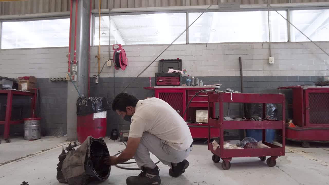 Latin male mechanic cleaning servicing engine parts on the floor at a workshop station in Puebla Mexico Latin-America