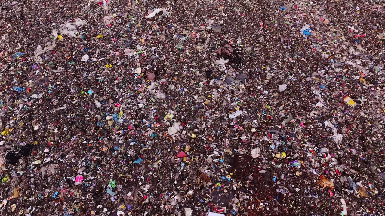 Plastiche colorate e detriti riempiono la superficie di una discarica, ripresa dall'alto, cupa e in movimento