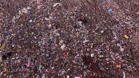 colorful plastics and debris fill landfill surface, grim top down tracking shot