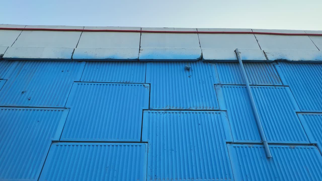 Panning shot of a highway overbridge wall built from large concrete blocks, painted blue, showing its texture and structure against a clear morning sky
